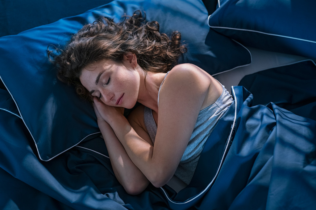 woman peacefully sleeping in a blue silky bed