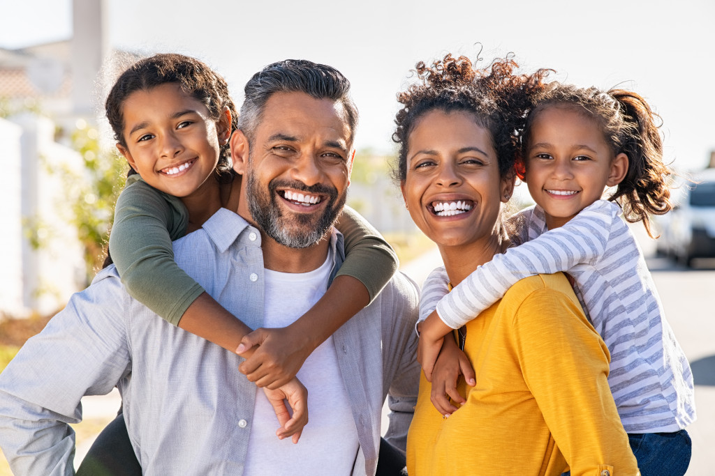 Mixed-race family at a park with the parents giving piggyback rides to their children.