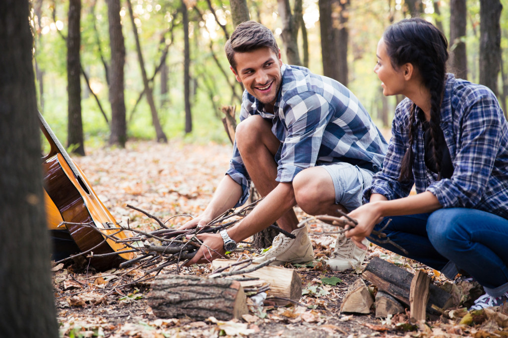 man and woman smiling while making fire in the forest