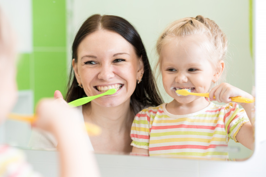 mother smiling while brushing teeth with daughter